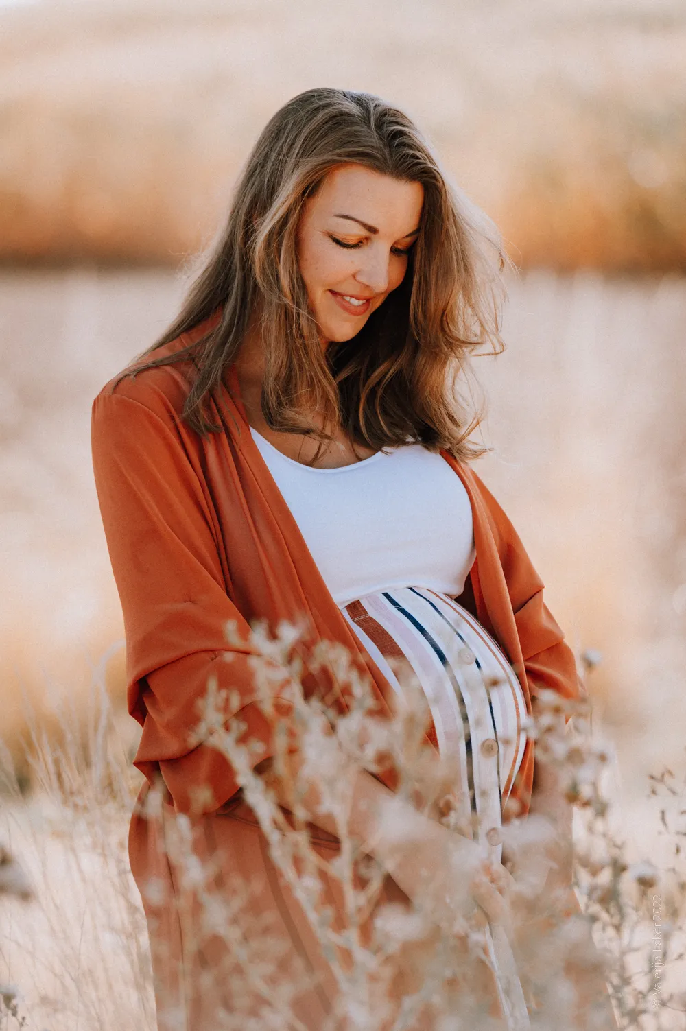 schwangere Frau schaut lächelnd auf ihren Babybauch in der freien Natur fotografiert von Valerija Ecker