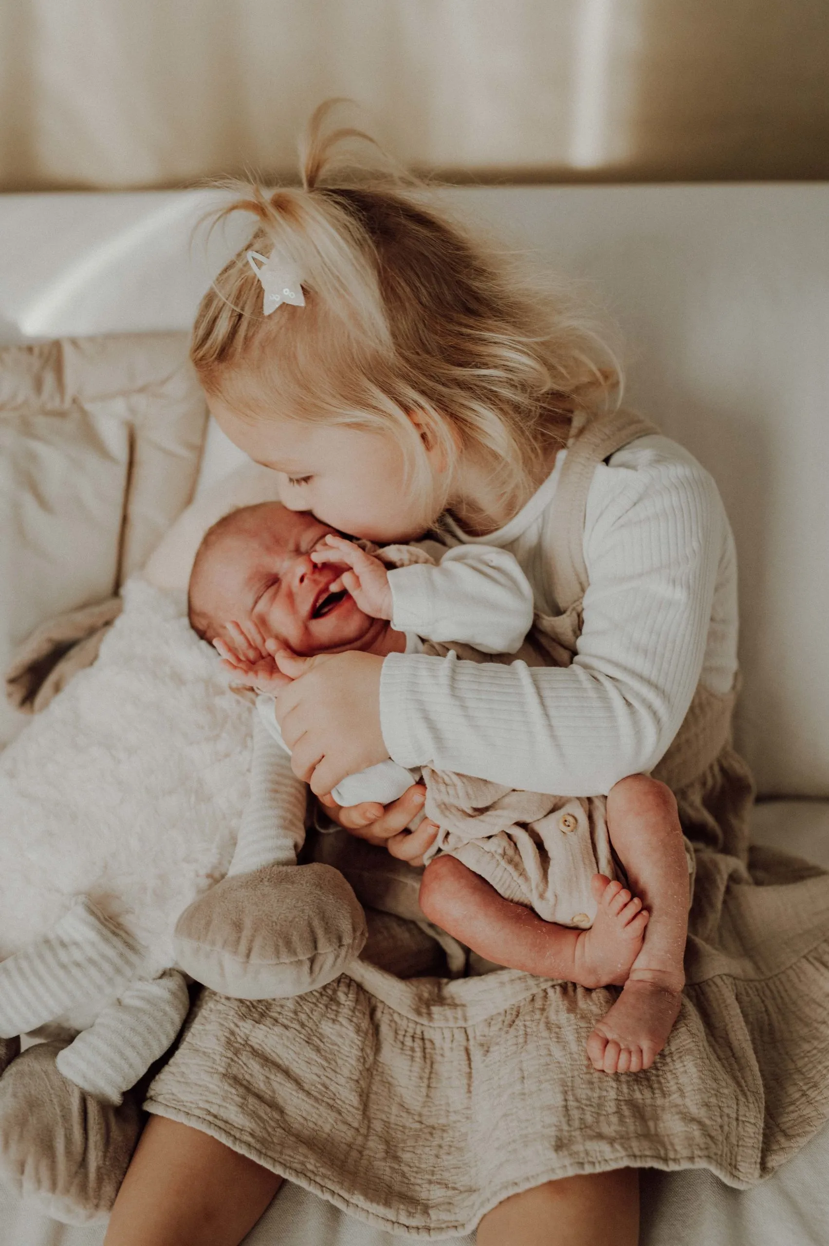 Kleines Mädchen hält ein Baby auf dem Schoß und küsst es fotografiert von Valerija Ecker